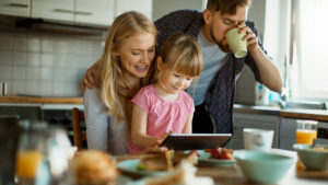 En mor, far og datter ser på en ipad rundt frokostbordet, illustrasjonsbilde.